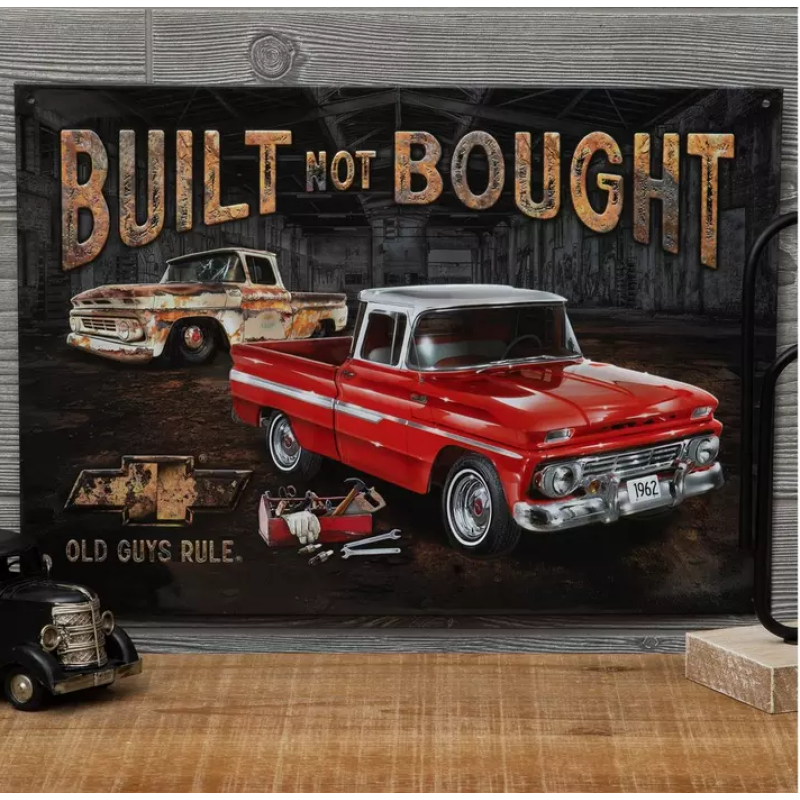 Decorative sign with vintage trucks and 'Built Not Bought' text on a wooden surface.