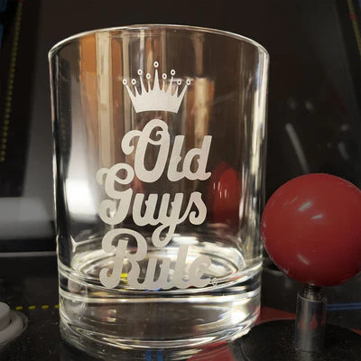 Clear glass tumbler with 'Old Guys Rule' engraving on a dark surface.