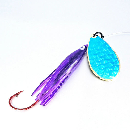 A fishing lure with a purple translucent skirt, a red hook, and a textured turquoise blue teardrop blade with a gold-colored edge, shown on a plain white background.